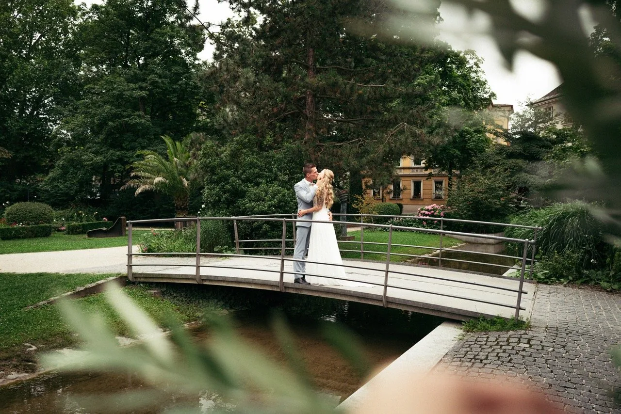 Brautpaar auf einer Bogenbrücke im Park, durch Blätter hindurch fotografiert