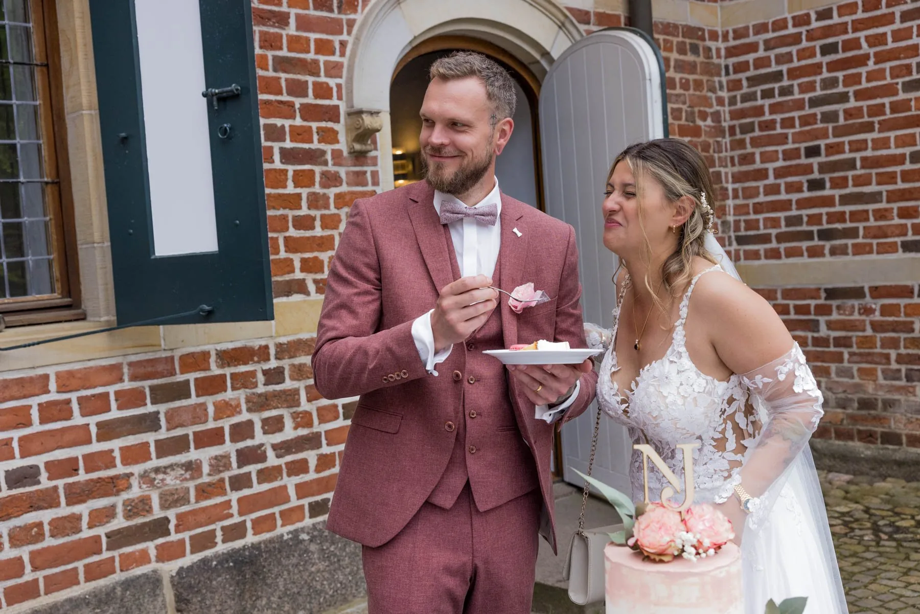 Der Bräutigam probiert ein Stück der Hochzeitstorte, die Braut sieht ihm dabei zu