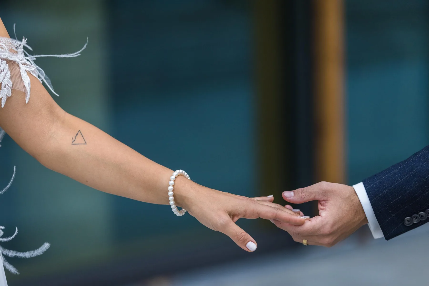 Die Hände von Braut und Bräutigam berühren sich mit den Fingerspitzen, am Handgelenk ein Perlenarmband