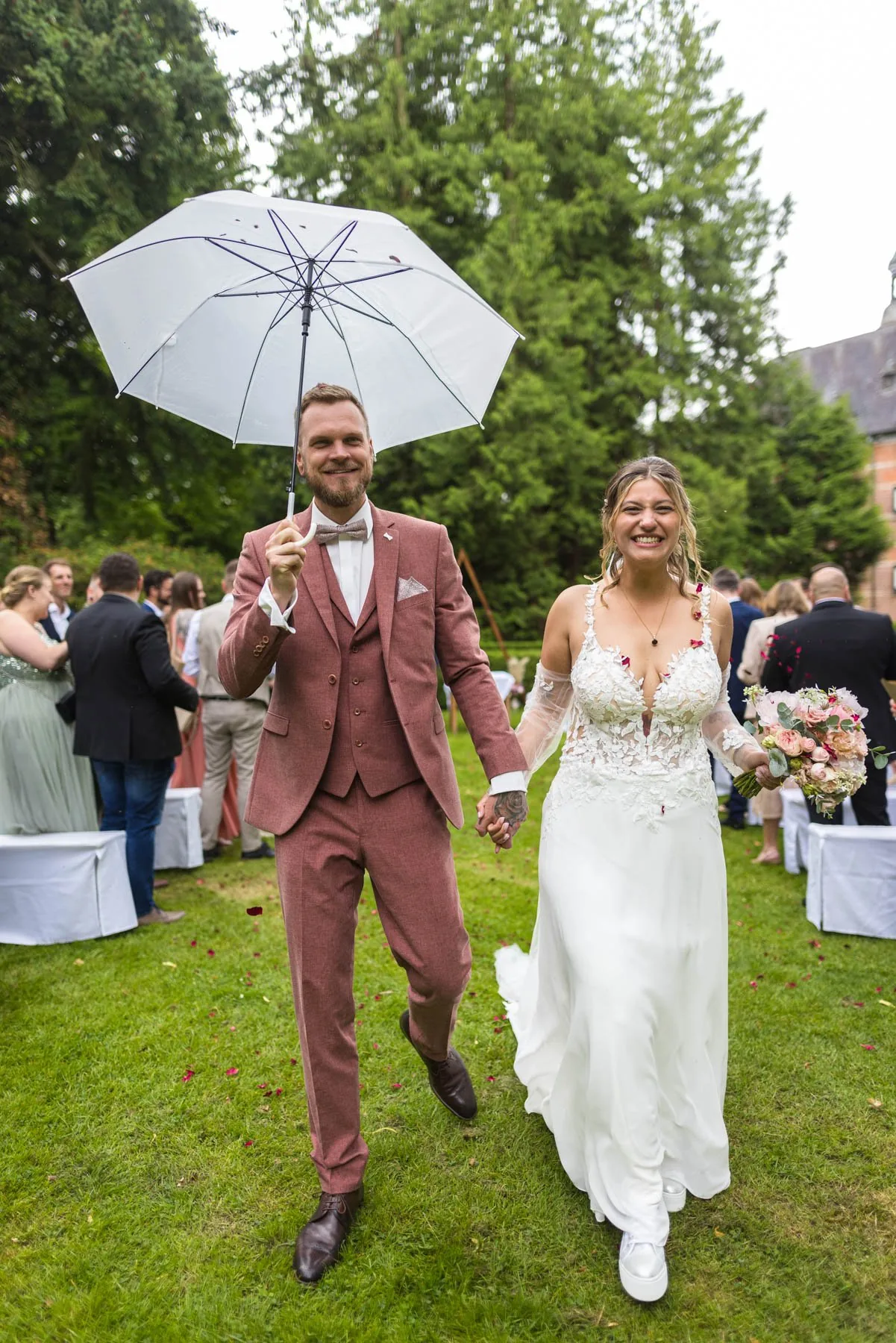 Jaci und Nils laufen mit einem aufgespannten Schirm durch ihre Gäste im Garten