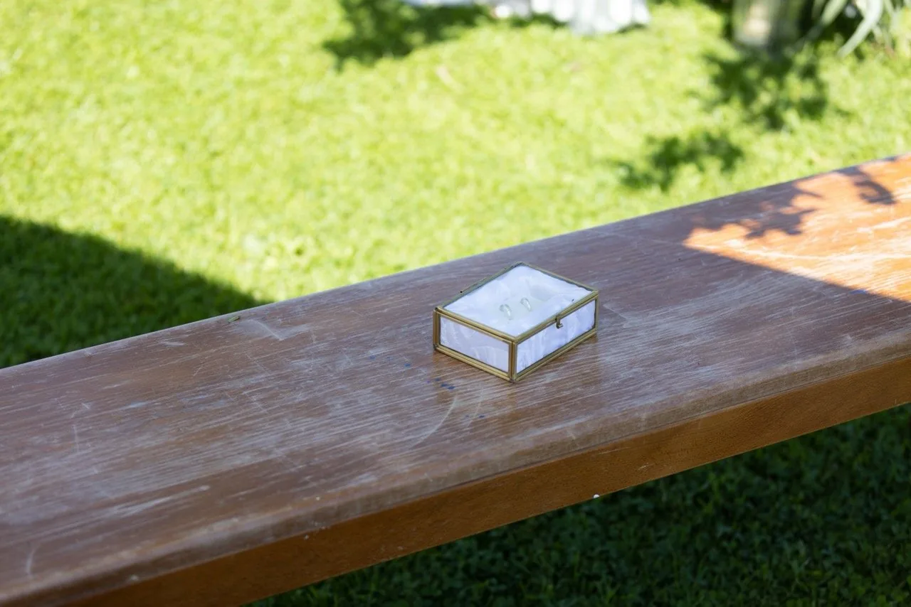 Die Ringschatulle aus Glas und Messing liegt auf einer Holzbank im Garten